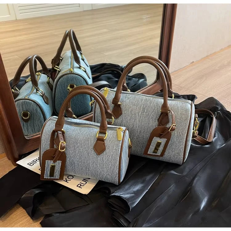Light denim cylinder handbags with brown leather handles, gold hardware, and luggage tags. Designer style purses.