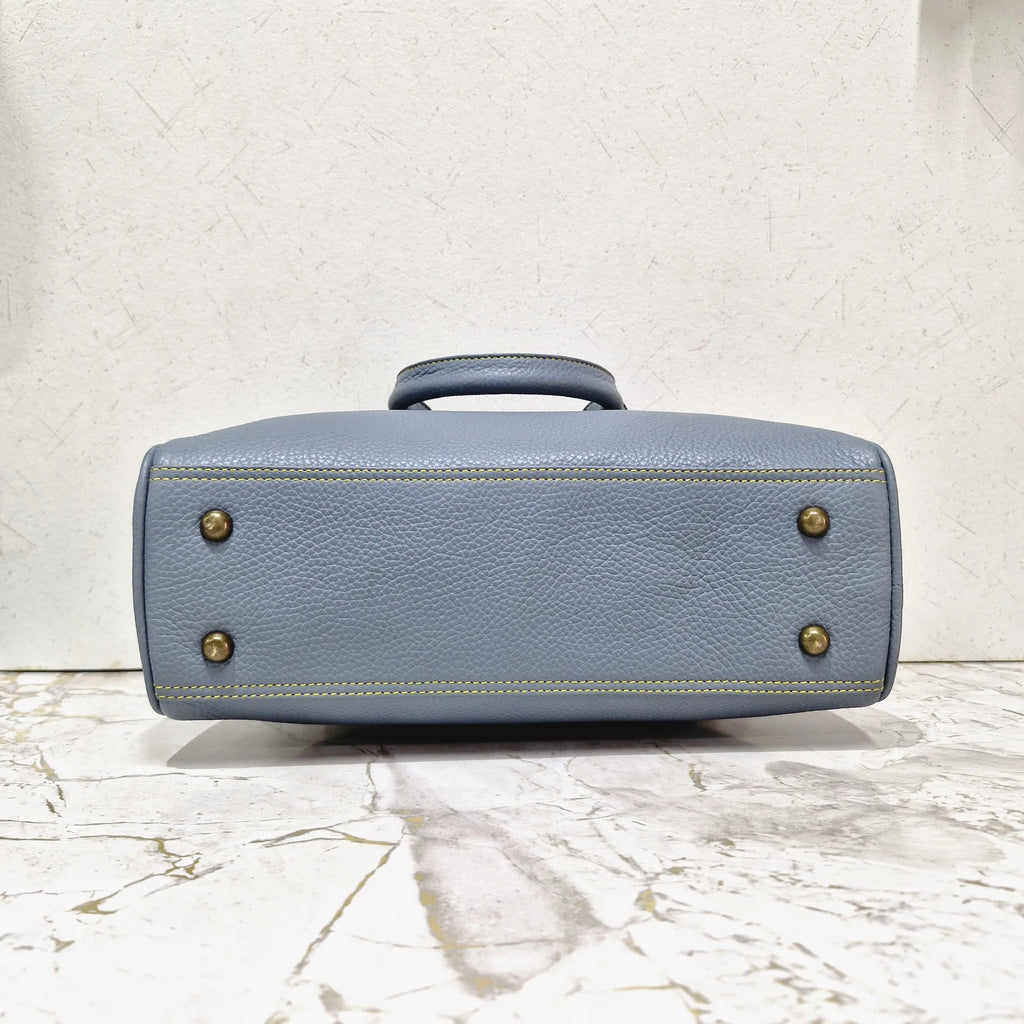 Blue genuine leather mini tote designer handbag with brass feet and contrast stitching on a marble surface.