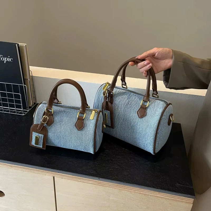 Light blue denim cylinder designer handbags with brown leather trim, gold hardware, and matching luggage tag detail.