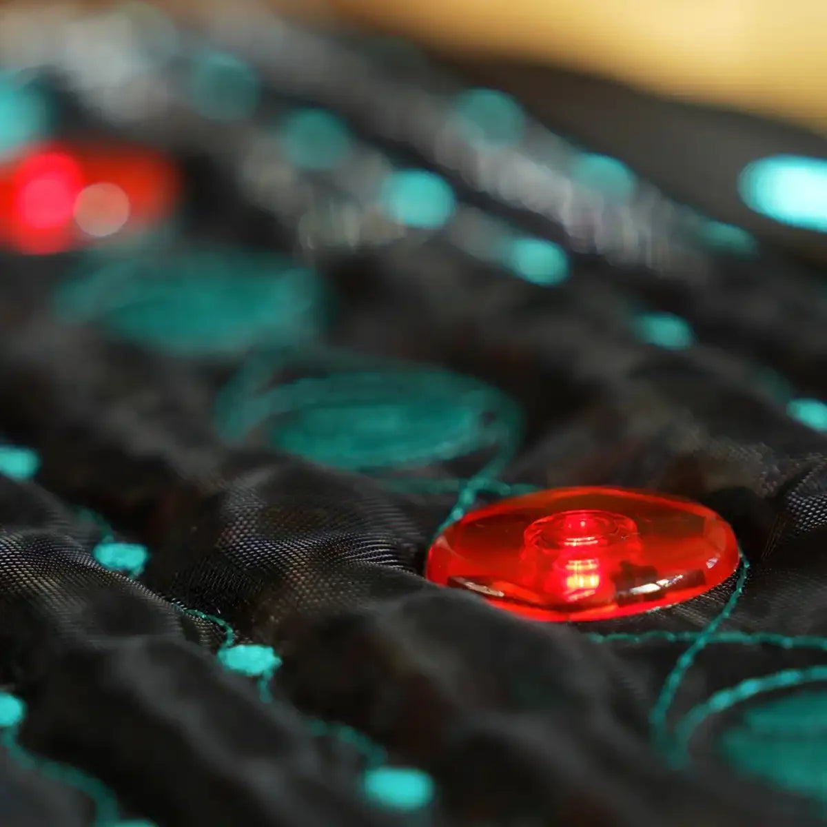 Infrared therapy mat with round red light stones embedded in a quilted black fabric surface.