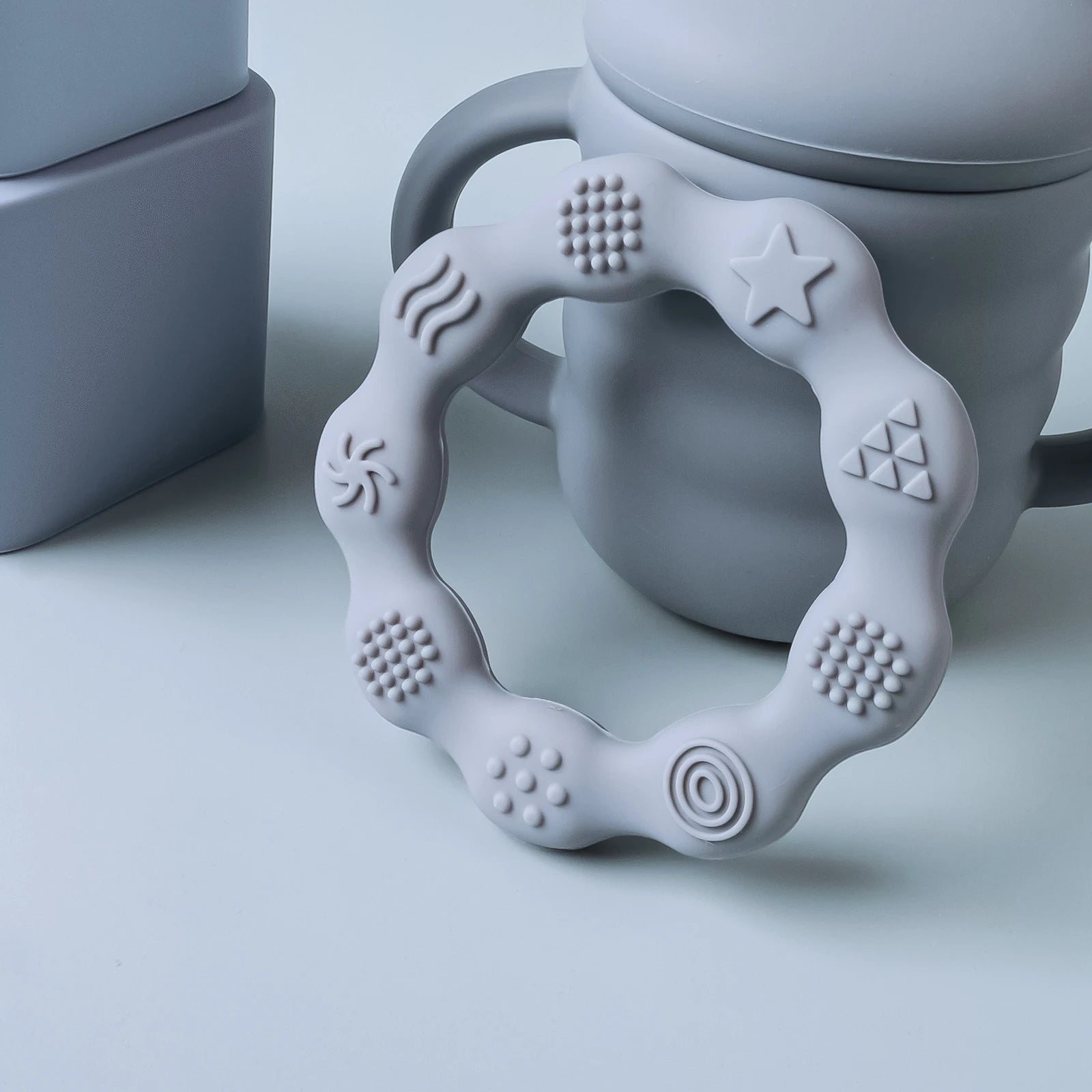 Grey silicone teething ring for baby relief, textured for sensory play.