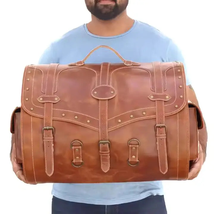 Large brown vintage leather trunk bag with buckle straps, brass stud detailing, and spacious design for travel.