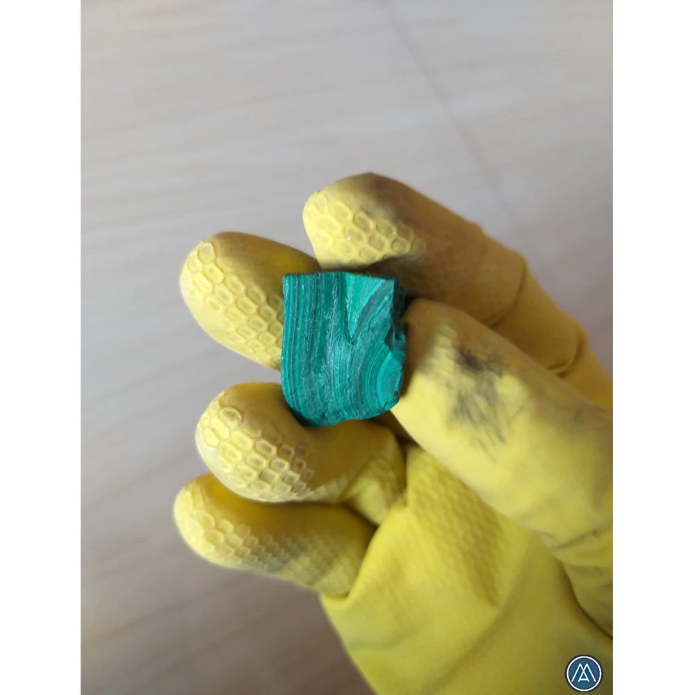 Raw teal-green malachite crystal piece held in a gloved hand