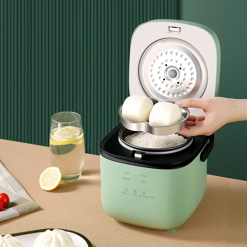 Mini electric rice cooker with green body and open lid, food tray with ingredients.