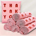 Pink polymailer mailing bag with heart print, stacked with rolled shipping bags