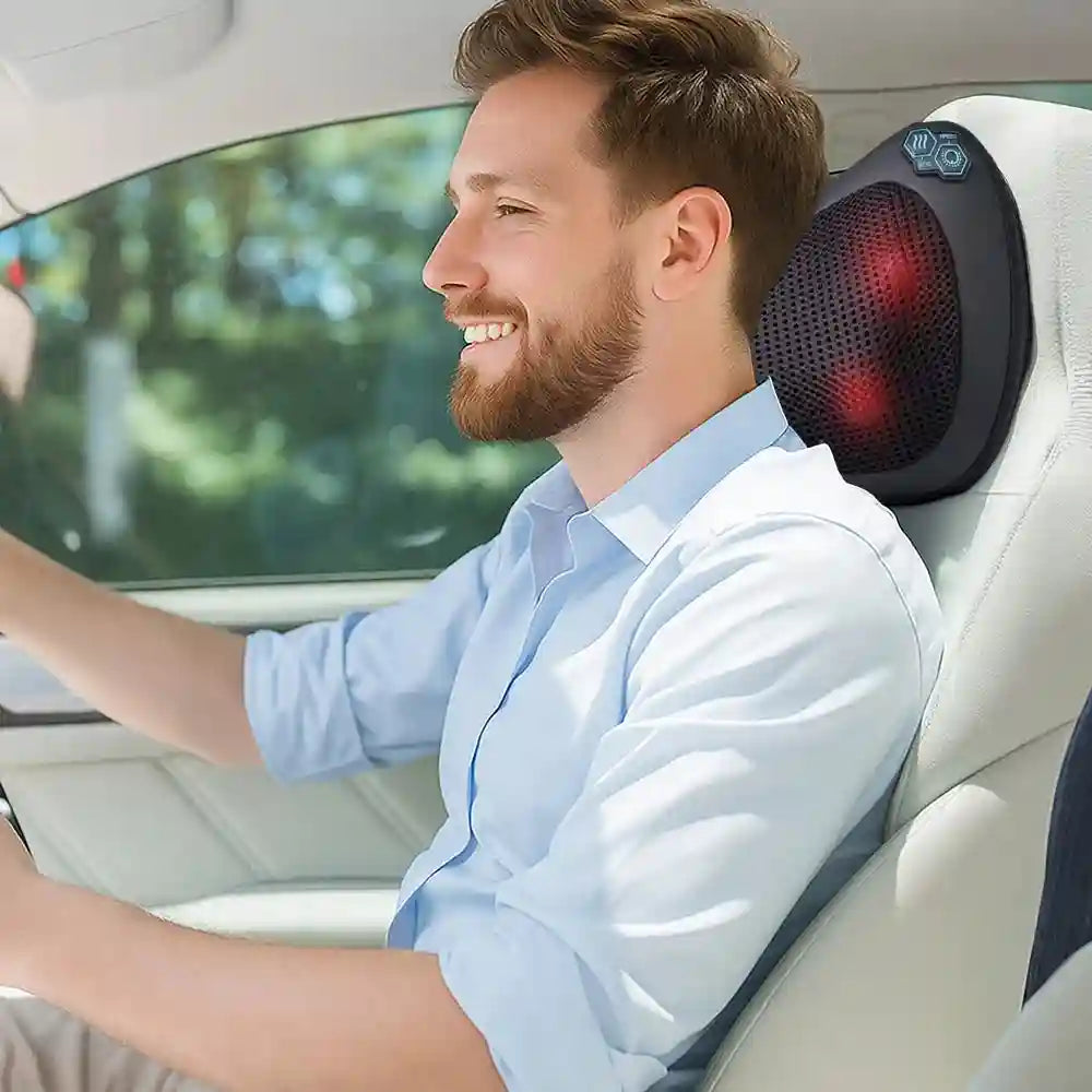 Man smiling while driving, using a black, mesh, shiatsu massage pillow with glowing red heat nodes on the headrest.