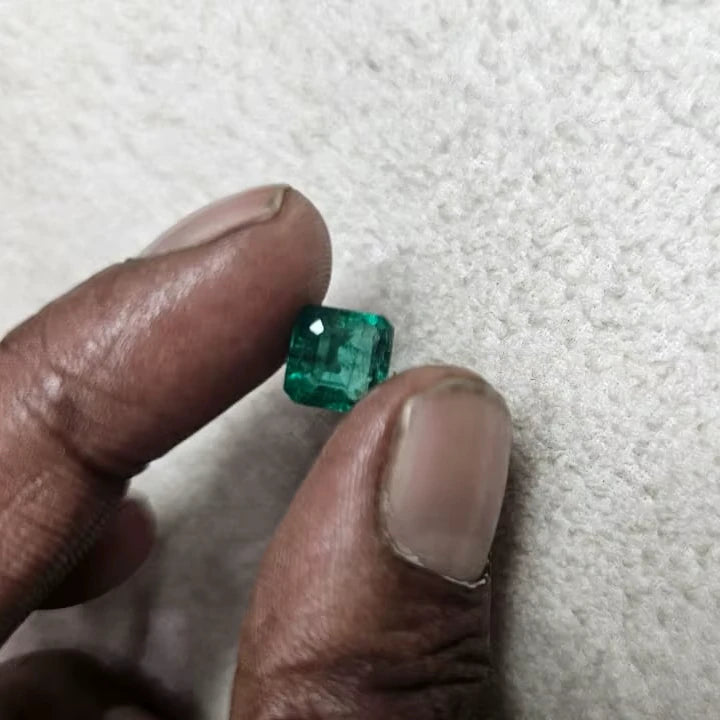 Green emerald-cut gemstone held between fingers, small rectangular cut on felt