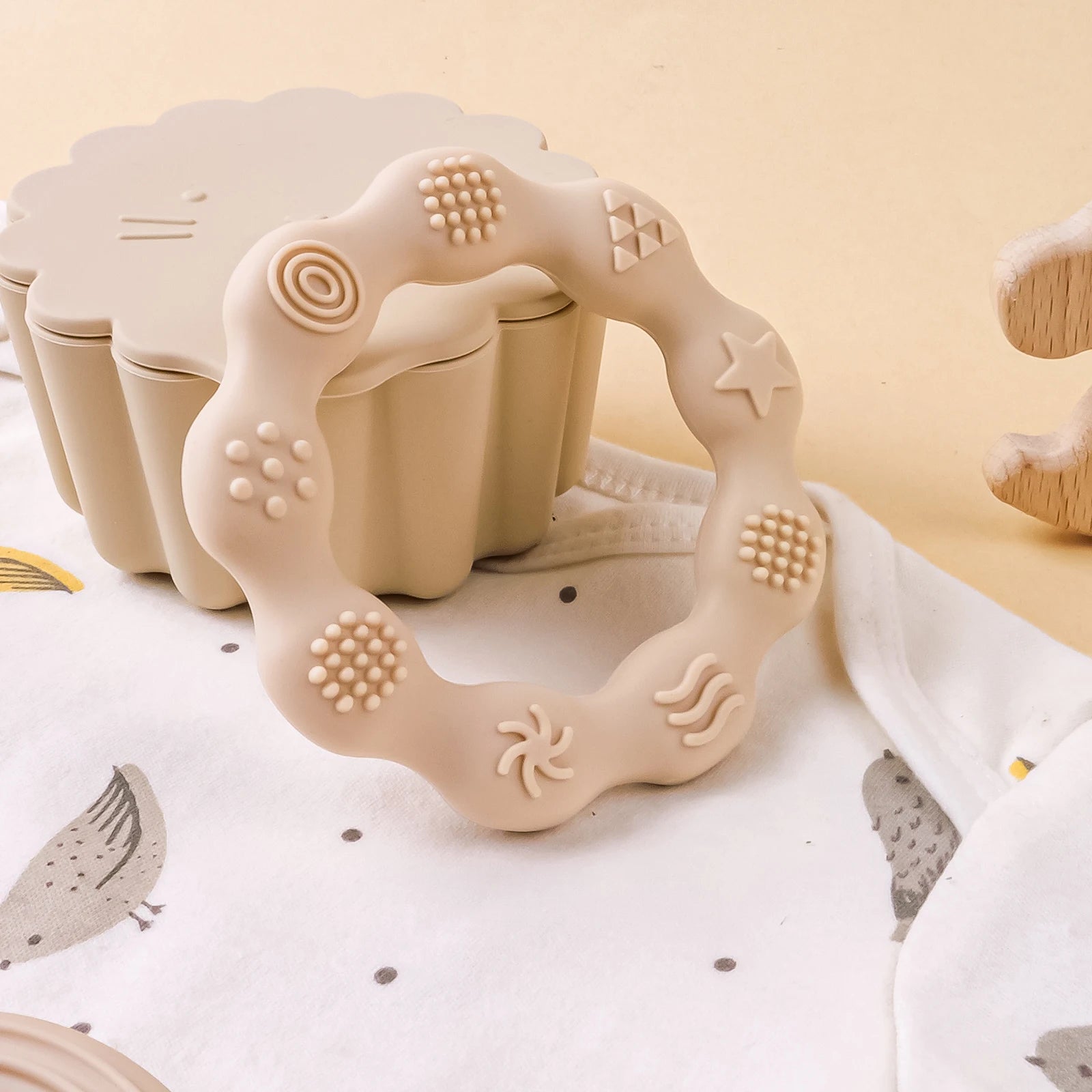 Beige silicone teething ring for baby relief with sensory textures.