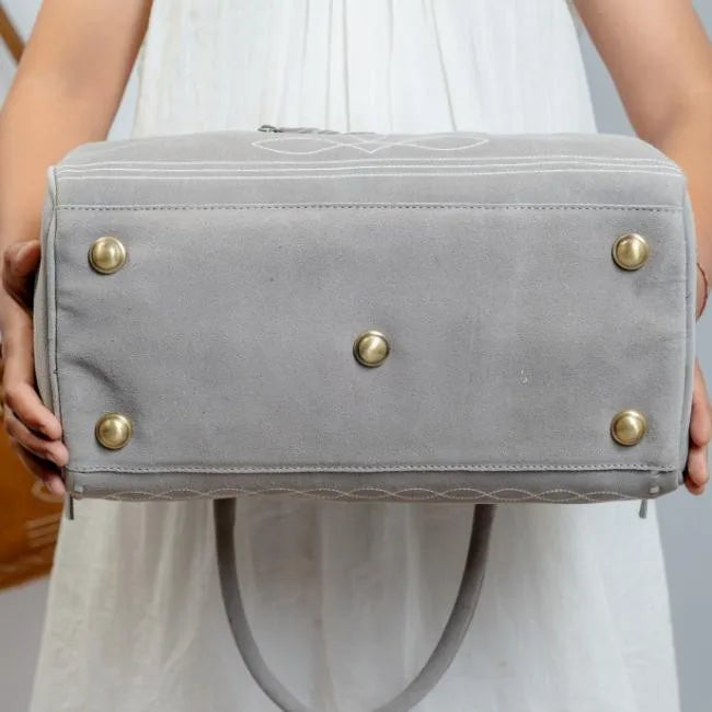 Grey handmade leather duffel trunk with brass feet, white boot stitch detailing, and durable construction for travel.