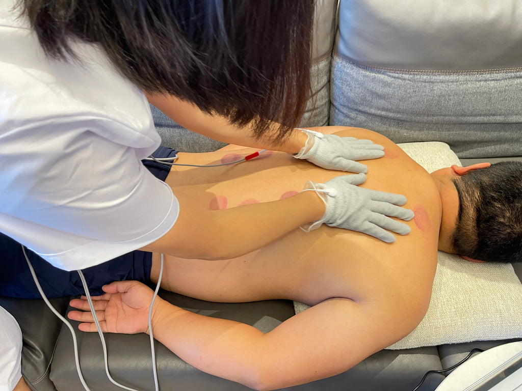 Therapist using a DDS bioelectrical body massager with conductive gloves for home electrotherapy on a man’s back.