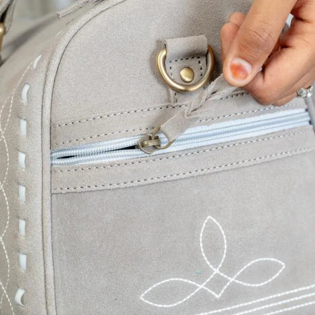 Grey suede leather duffel trunk with elegant white boot stitch detail, brass hardware, and zipper side pocket.