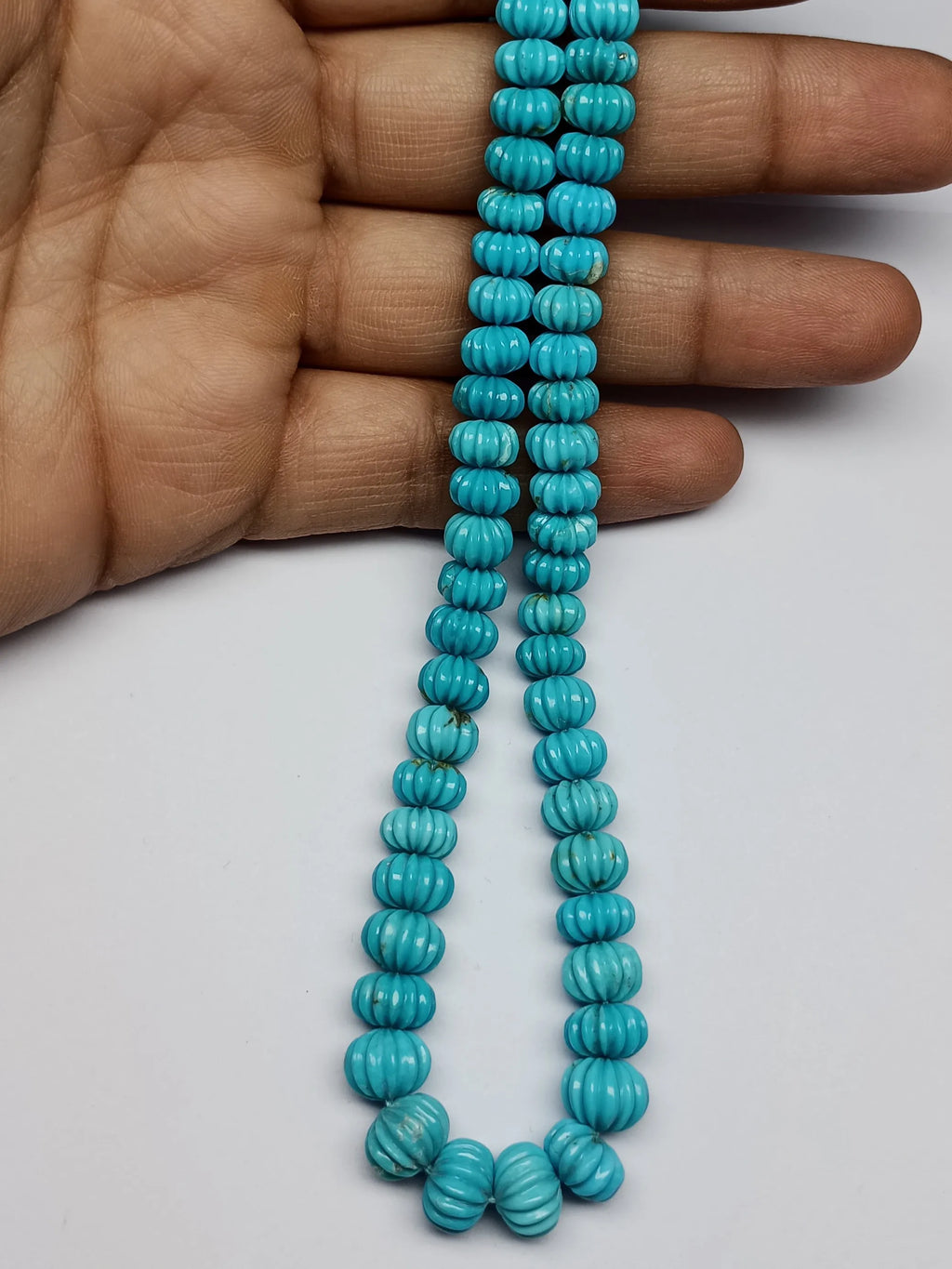 Blue turquoise carved pumpkin-shaped bead strand held in hand, small ribbed beads