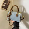 Light blue denim cylinder handbag with brown leather trim and top handles. Luxury designer casual barrel purse.