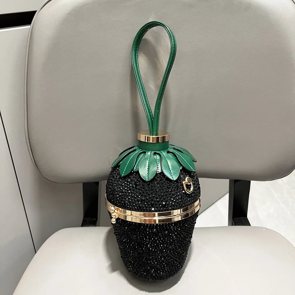 Black rhinestone strawberry-shaped evening clutch with a green leather leaf handle and gold-tone metal hardware.