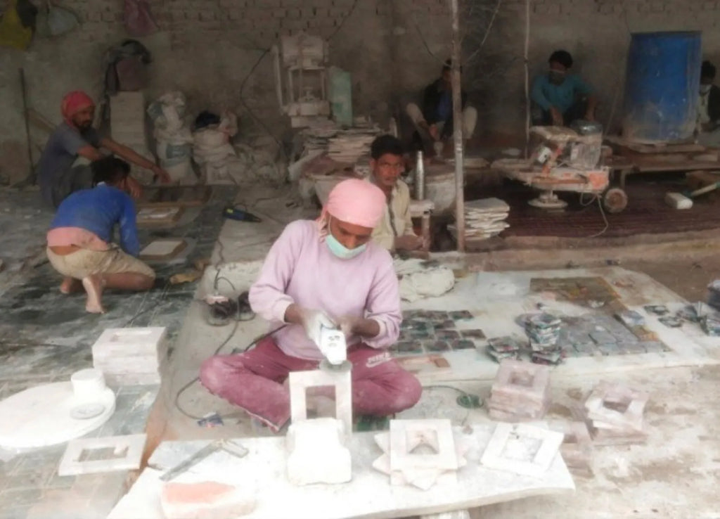 Worker shaping materials at a crafting table with tools and stone pieces