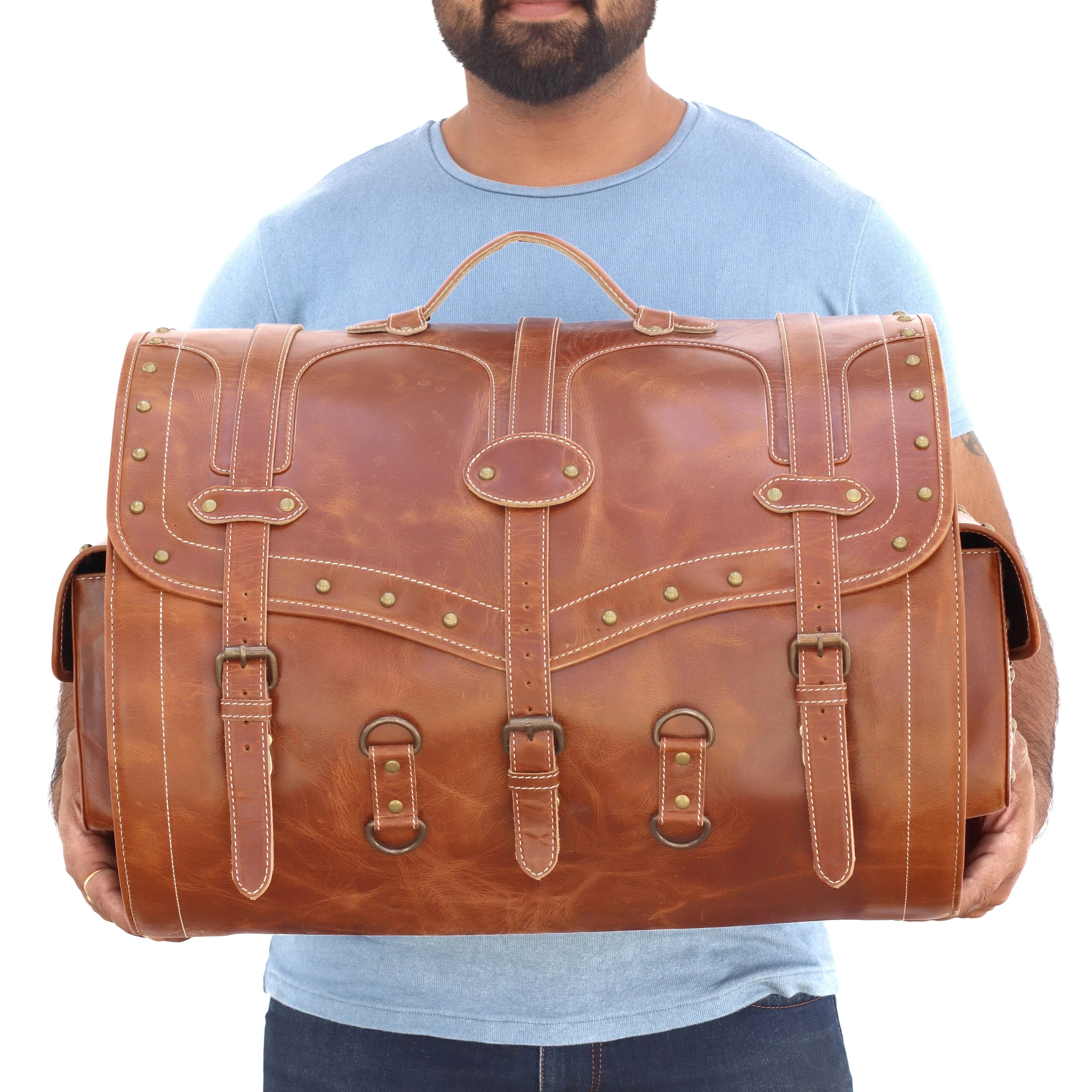 Large vintage brown leather trunk bag for travel with brass buckle straps, rivet detailing, and heavy-duty top handle.