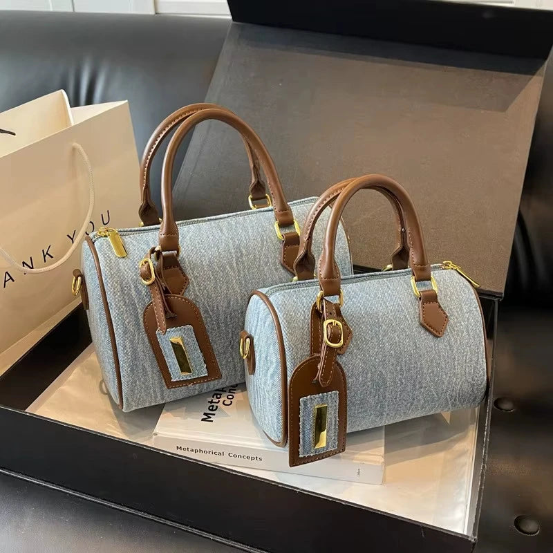 Designer denim cylinder handbags with brown leather handles, gold hardware, and matching luggage tags.