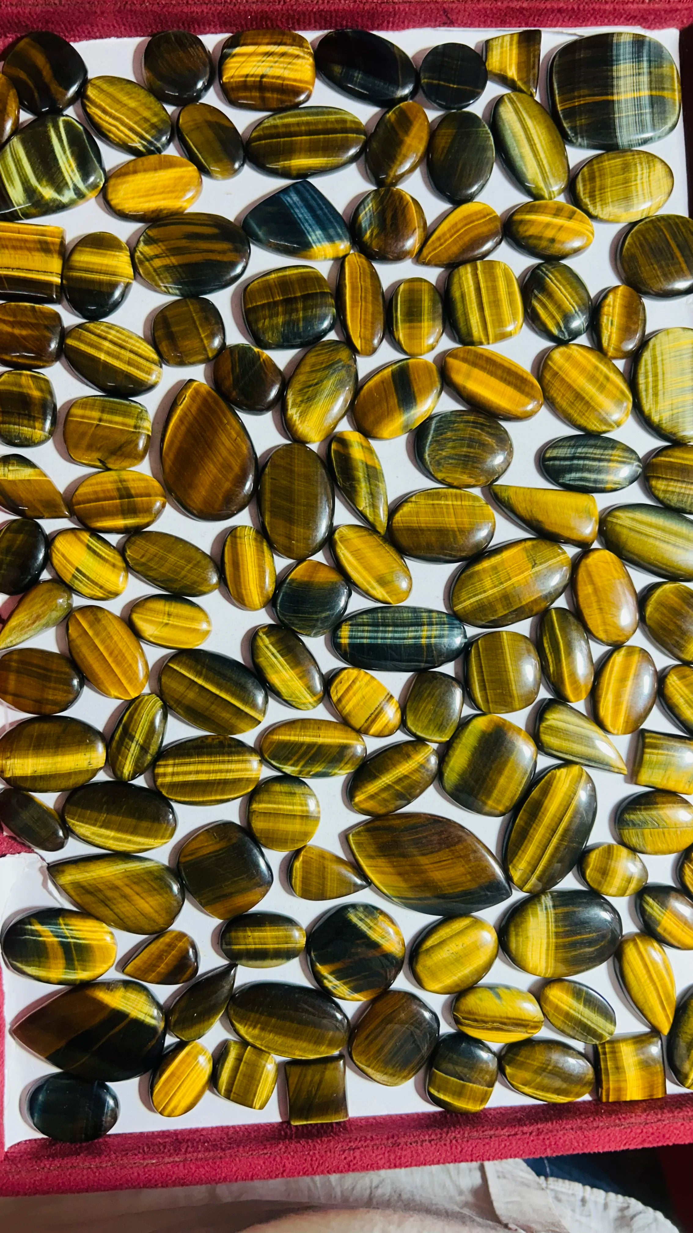 Mixed striped cabochon gemstones with yellow and dark green bands on red cloth
