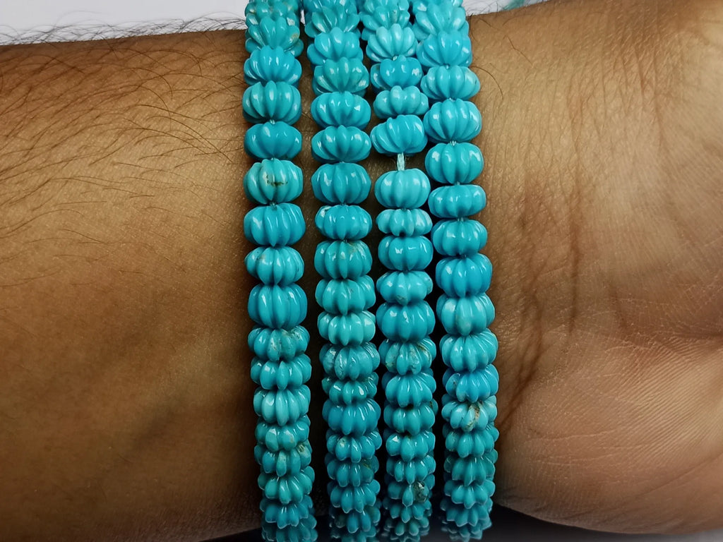 Blue turquoise carved pumpkin-shaped beads stacked on wrist, small ribbed beads
