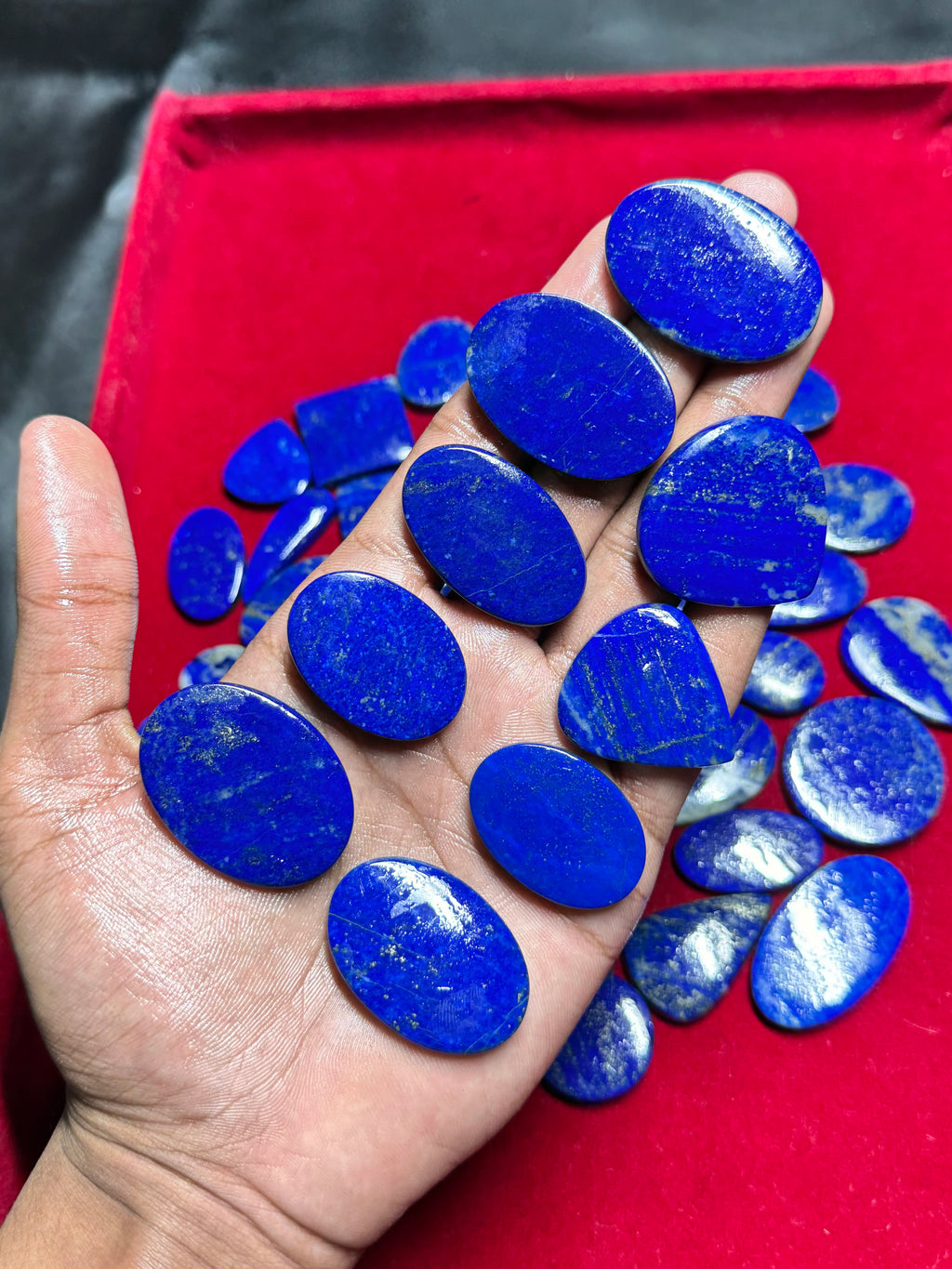 Smooth blue lapis lazuli cabochon gemstones, blue ovals in palm, loose pieces