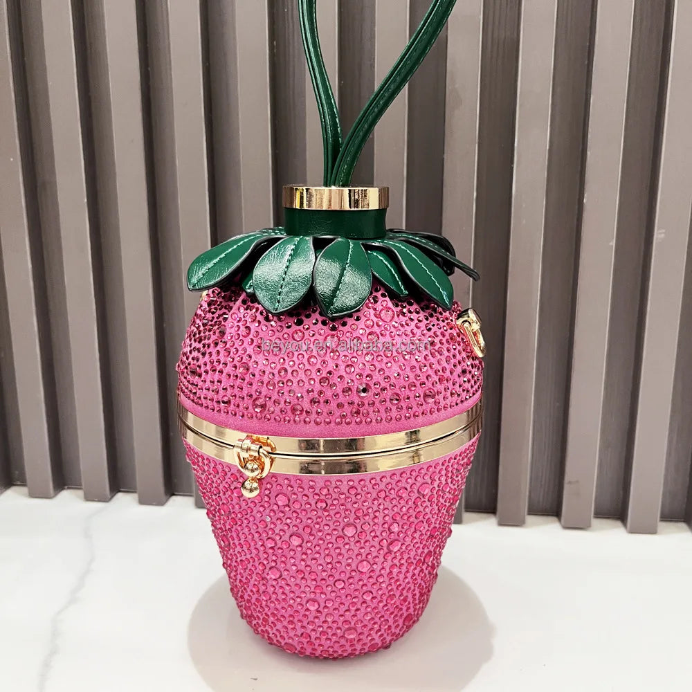 Pink strawberry-shaped luxury designer handbag covered in rhinestones with green leaf accents and a gold metal frame.