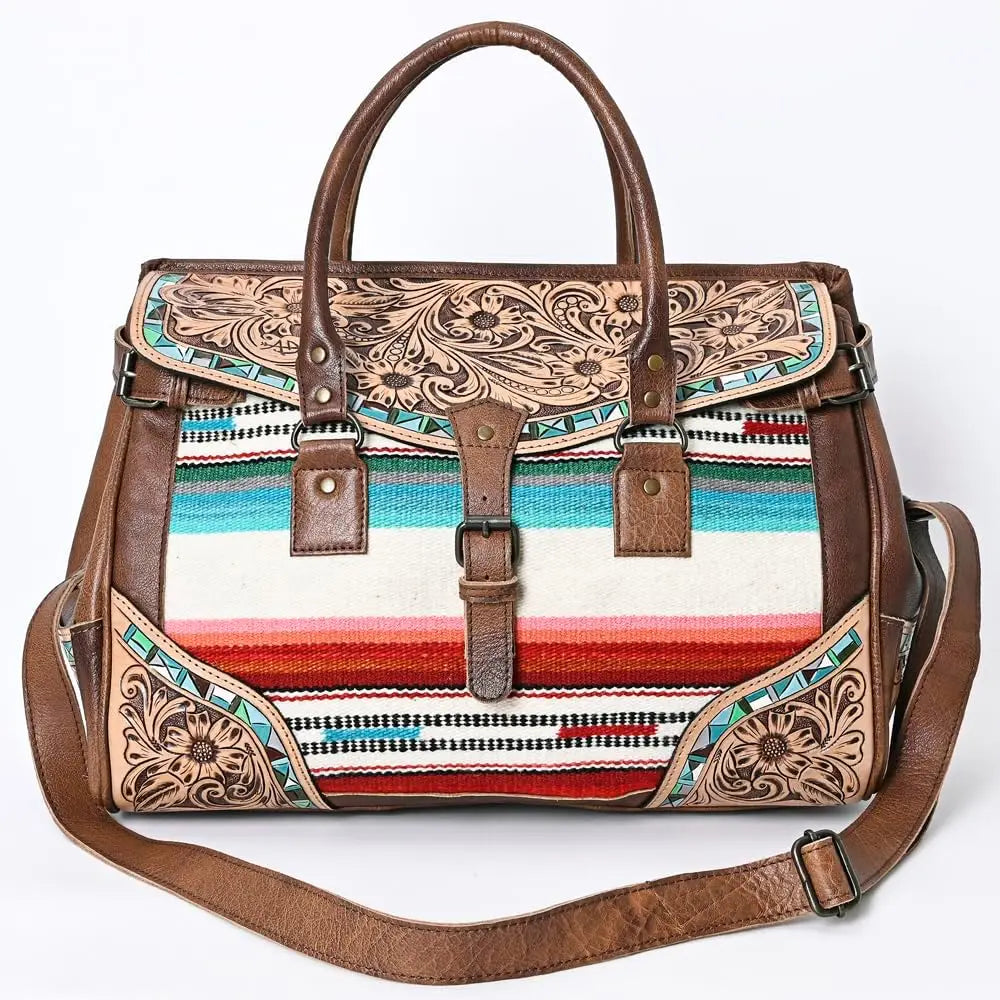 Handwoven leather duffel trunk with western floral tooling, colorful striped fabric, and adjustable shoulder strap.