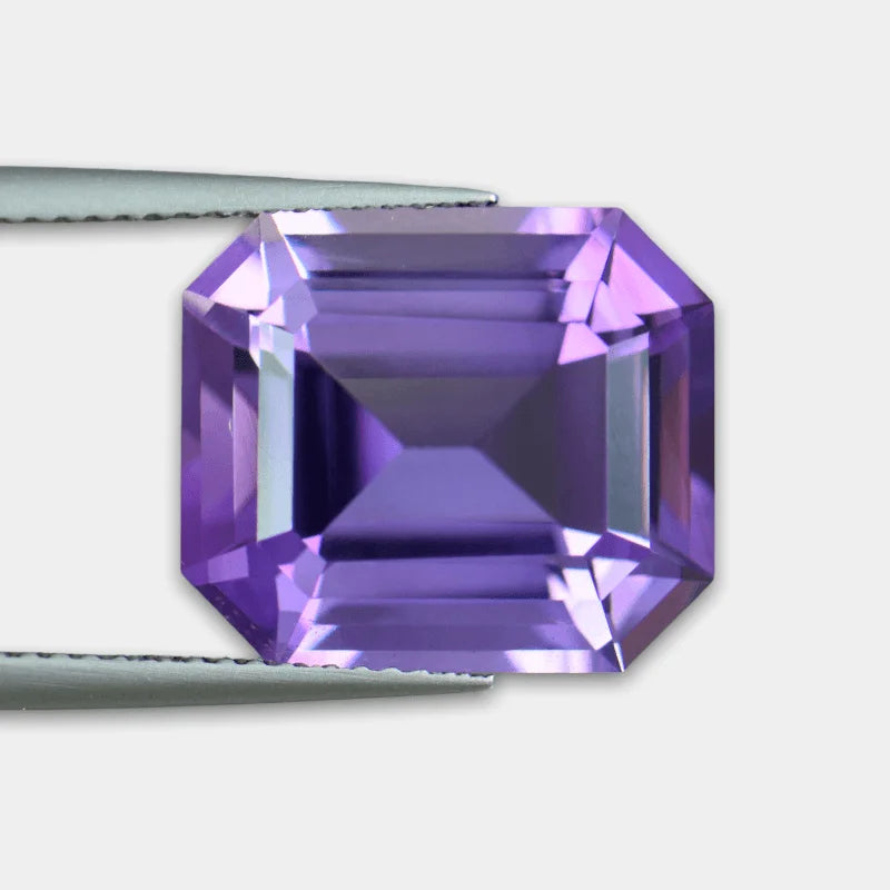 Close-up of emerald-cut purple amethyst gemstone held with metal tweezers