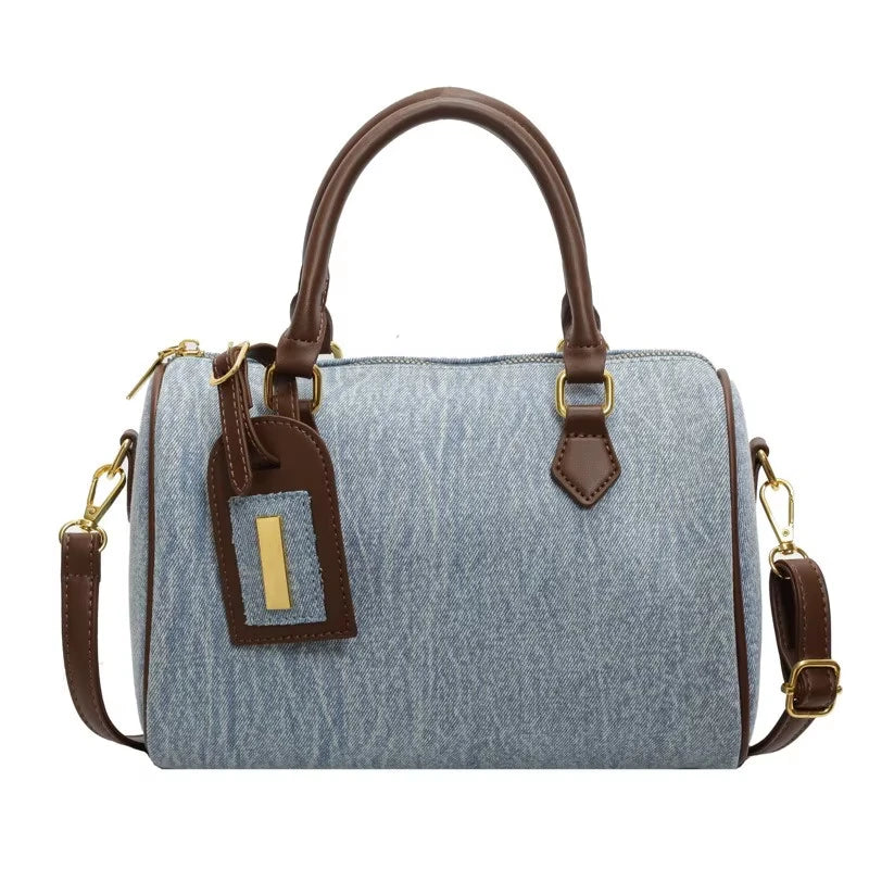 Light blue denim cylinder designer handbag with brown leather handles, shoulder strap, and gold-tone hardware.