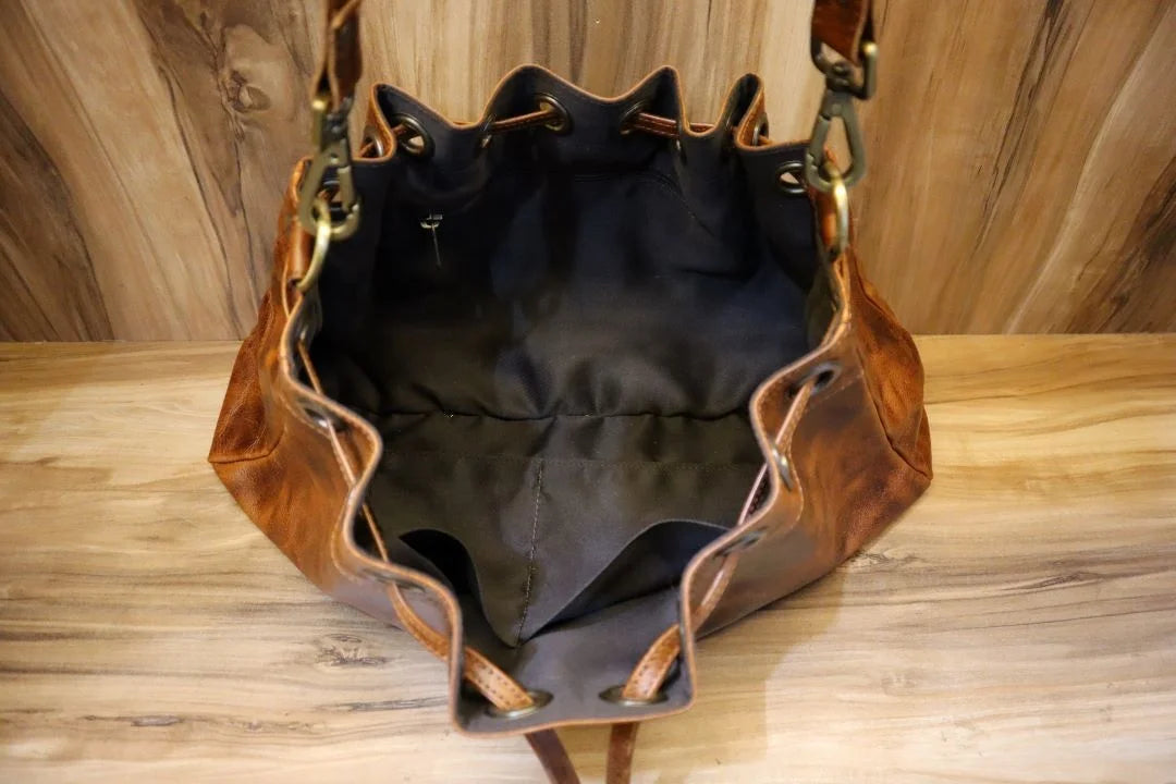 Brown distressed leather bucket shoulder bag with drawstring closure, metal hardware, and lined interior pockets.