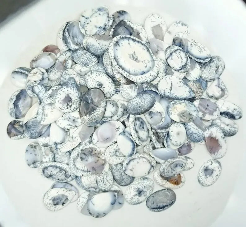 Scattered oval dendrite opal cabochon stones, white with black speckle patterns