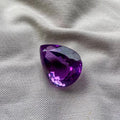 Amethyst gemstone, pear cut with deep purple facets and sparkling reflections