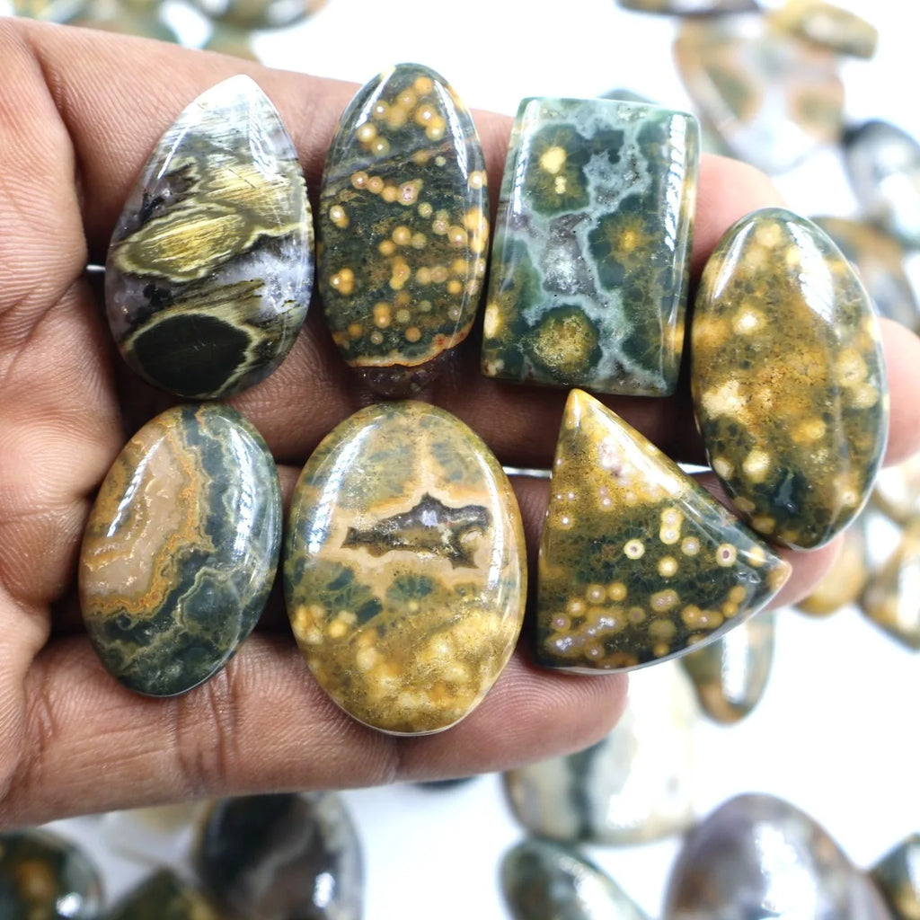 Hand holding ocean jasper cabochons, oval and curved shapes with green, gold, and black druzy specks