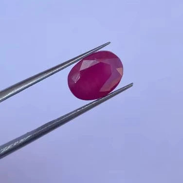 Oval faceted red gemstone held with metal tweezers