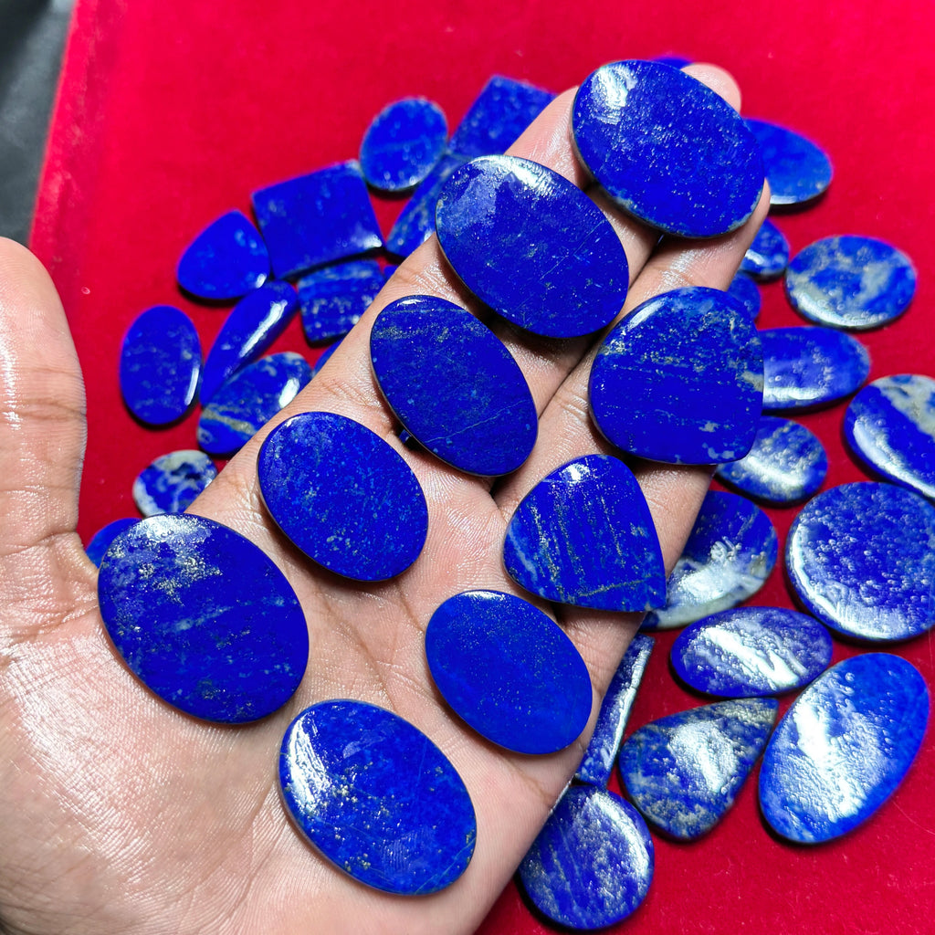 Smooth blue lapis lazuli cabochon gemstones, oval stones in hand, loose assortment