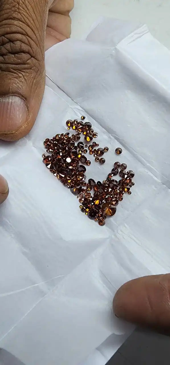 Loose faceted lab-grown diamond stones in brown and dark blue mix, held in hand