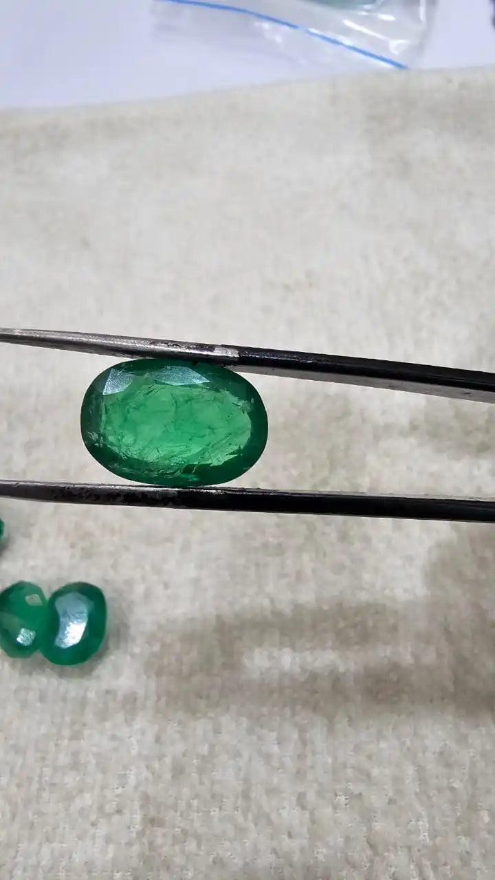 Polished green oval emerald-cut gemstone held between tweezers