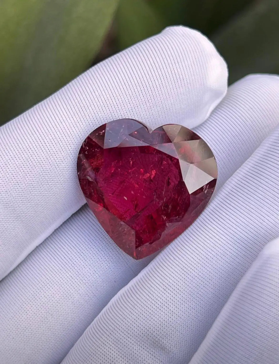 Heart-shaped faceted red gemstone in white gloves