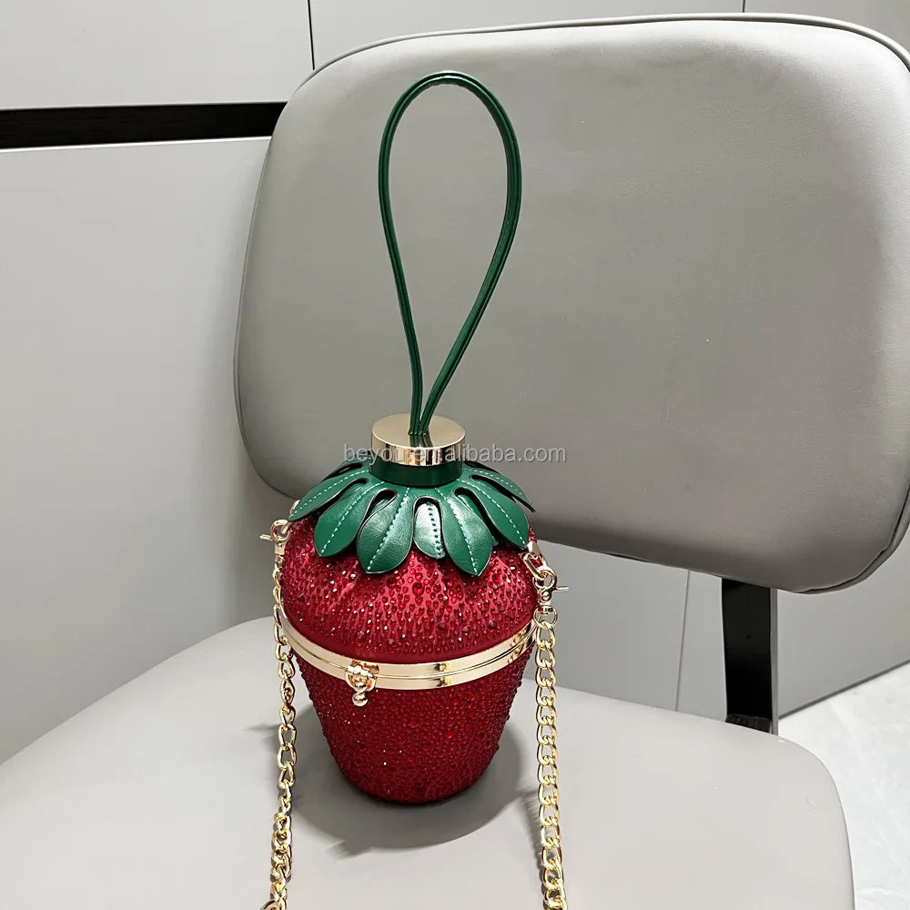 Red rhinestone strawberry evening clutch with green leaf top, gold chain strap, and luxury designer bucket bag style.