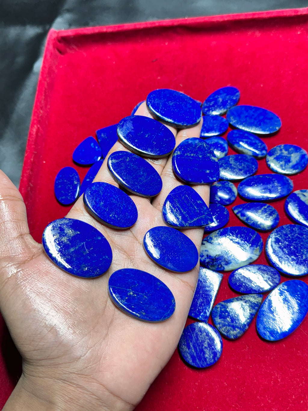 Smooth blue lapis lazuli cabochon gemstones, oval stones and small drops in hand