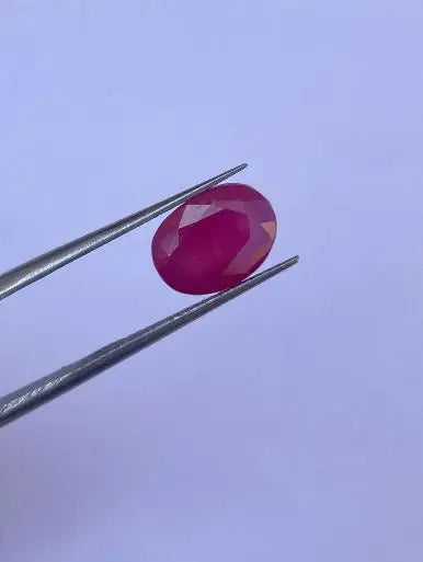 Oval faceted red gemstone on metal tweezers, close-up
