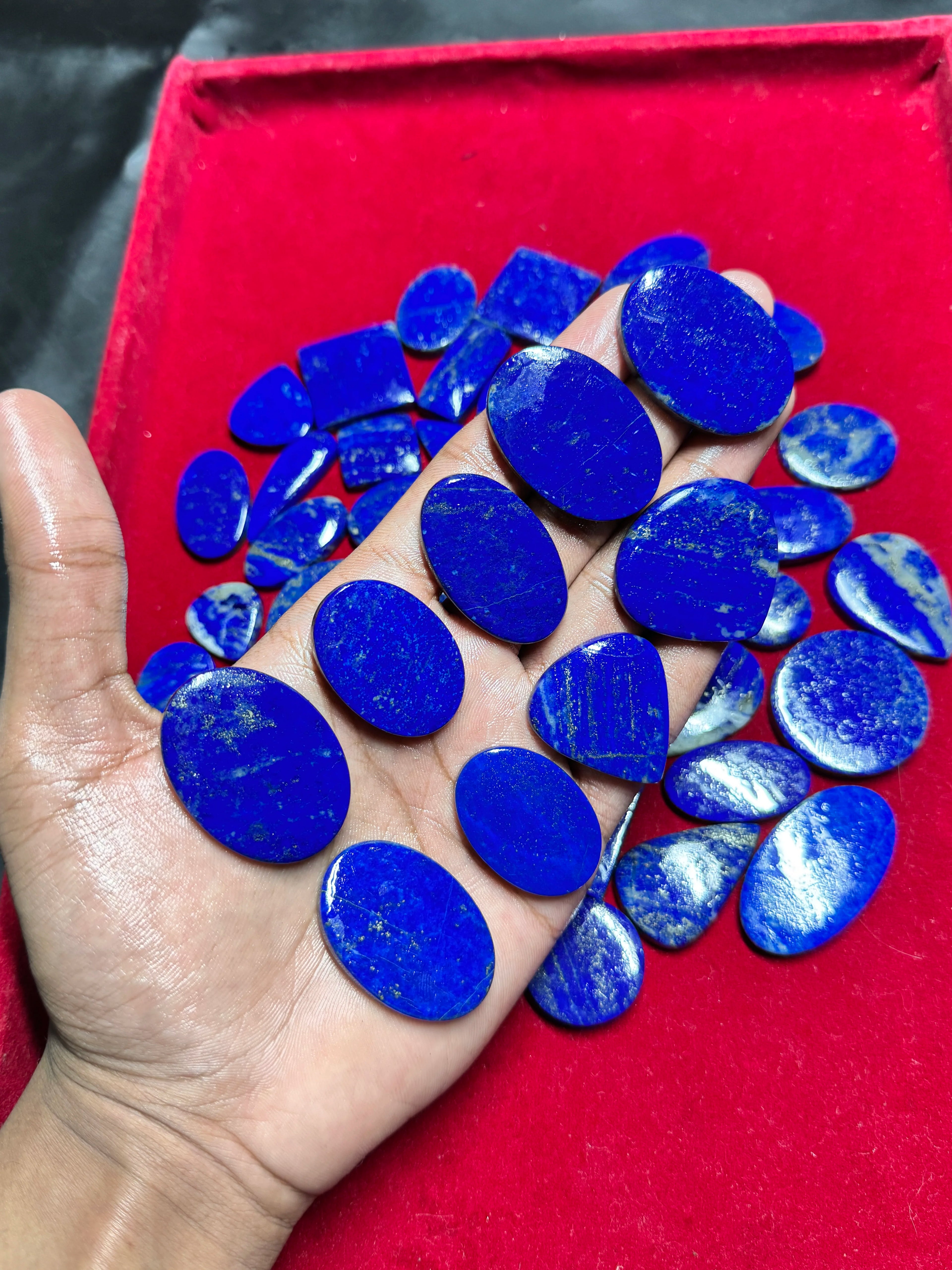 Smooth blue lapis lazuli cabochon gemstones, mixed oval shapes in open hand
