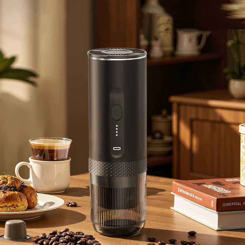 Portable matte black electric coffee maker with clear base and LED power indicator on a wooden tabletop.