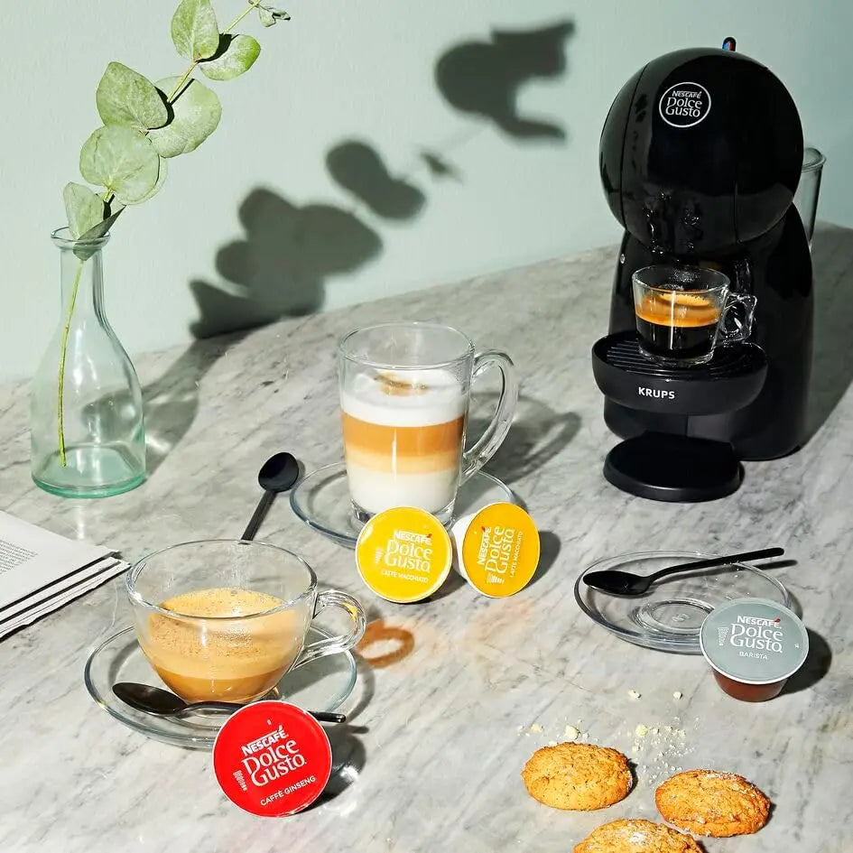 Black Krups Nescafé Dolce Gusto pod coffee machine brewing espresso with various coffee capsules on marble table.
