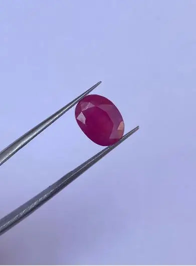 Oval faceted red gemstone between metal tweezers