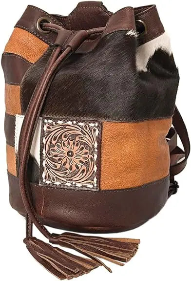 Western bucket bag in patchwork leather and cowhide with tooled floral detail, drawstring closure, and tassel accents.