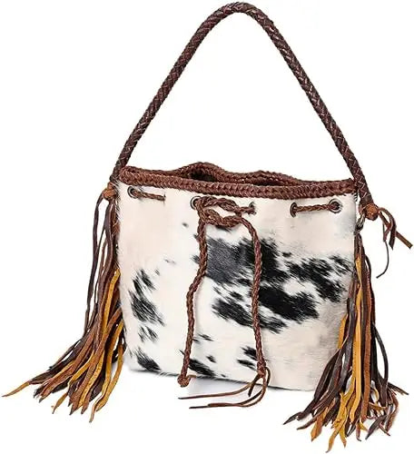 Trendy black and white cowhide bucket bag with brown braided strap and long fringe side accents in a western style.