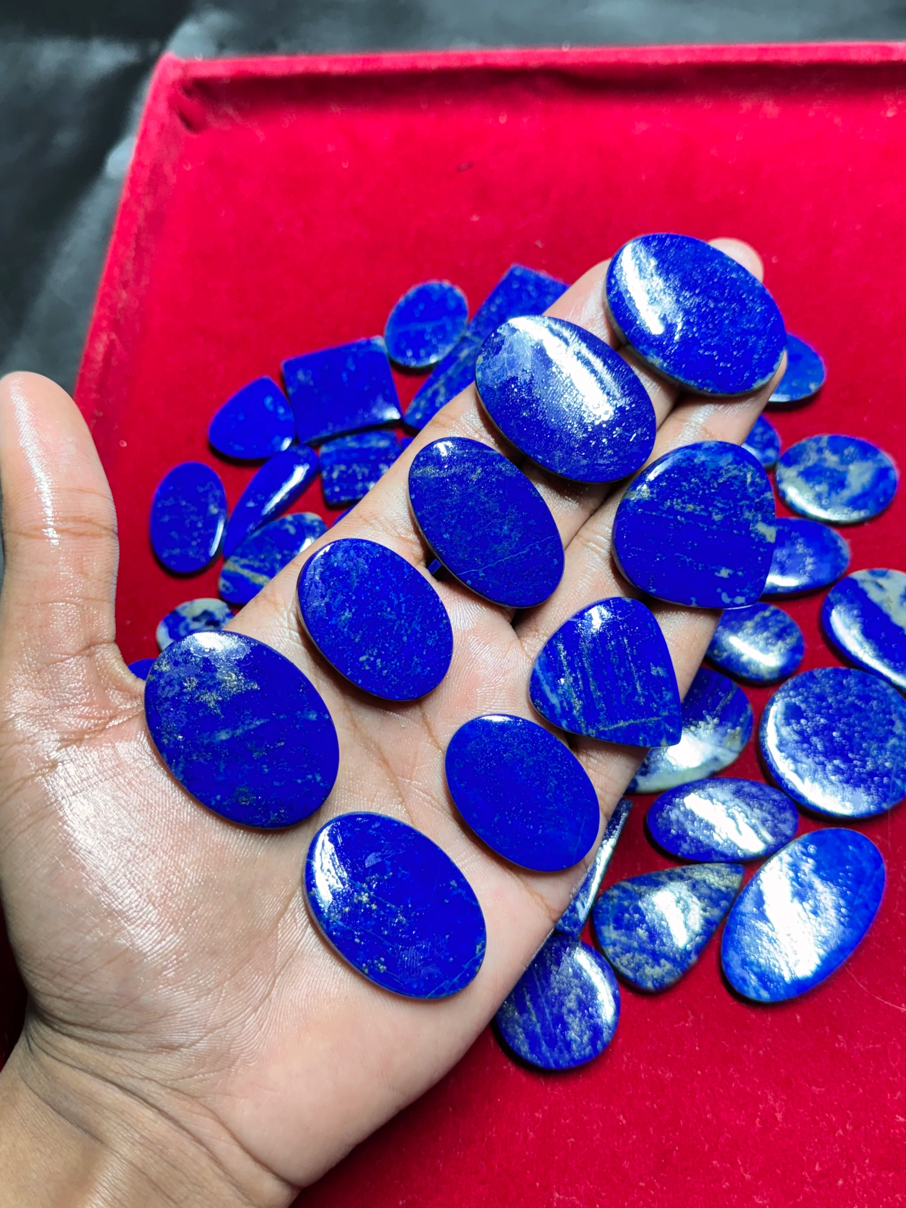 Smooth blue lapis lazuli cabochon gemstones, polished ovals and small chips in hand