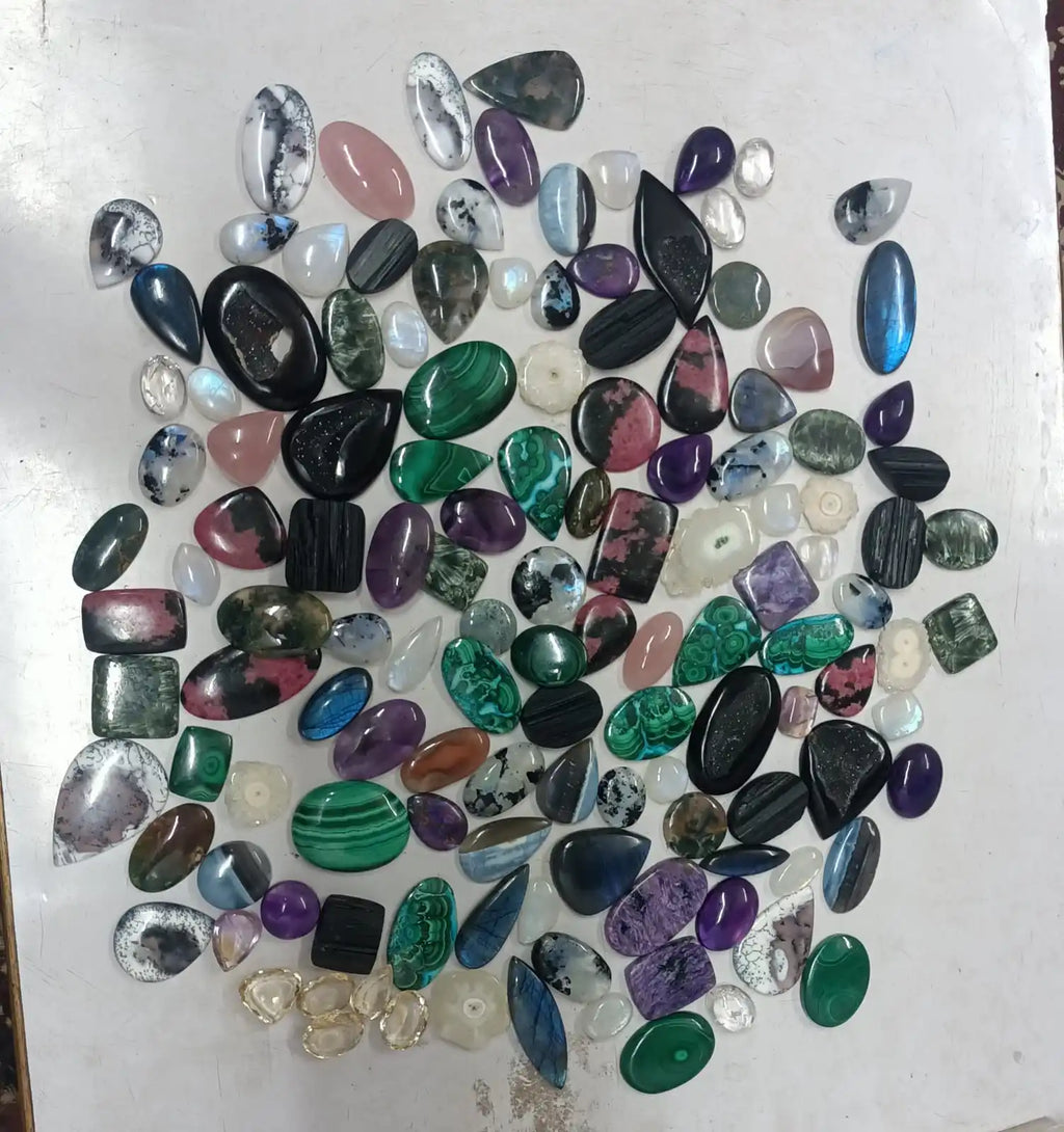 Mixed-shape cabochon gemstone assortment with oval stones in purple, green, and dark tones