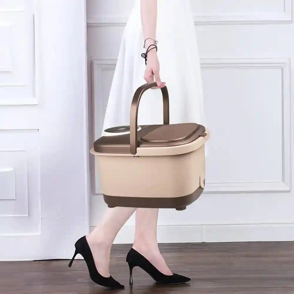 A person carrying a beige and brown automatic massage foot spa with a handle and digital control panel.