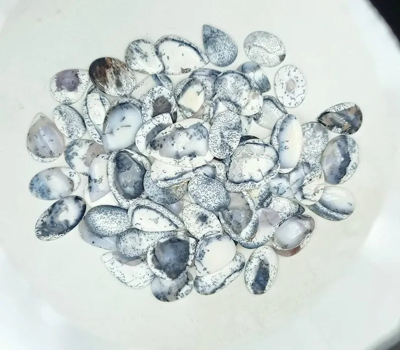 Dense scatter of oval dendrite opal cabochon stones, white with black speckles